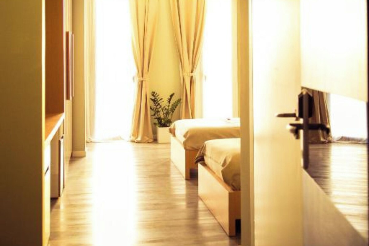 A hotel room with a bed, a bedside table, a plant, and a window with curtains.