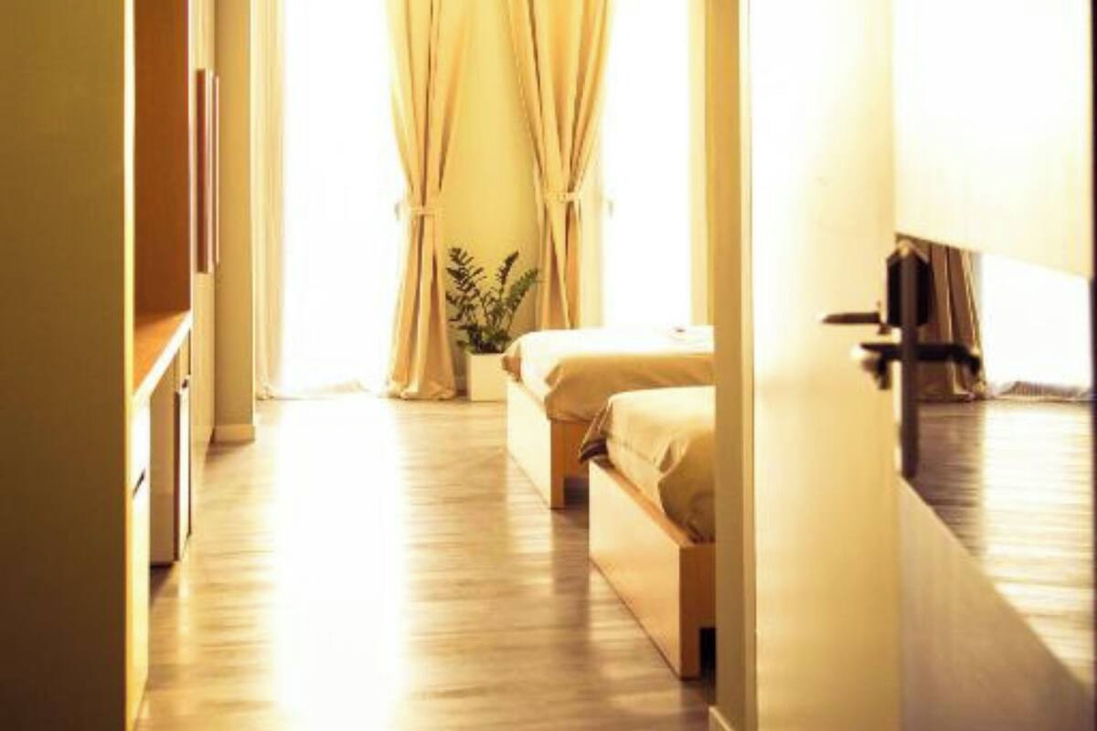 A hotel room with a bed, a bedside table, a plant, and a window with curtains.