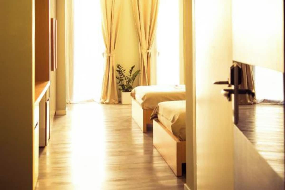 A hotel room with a bed, a bedside table, a plant, and a window with curtains.