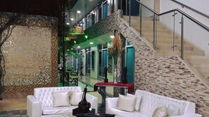 A modern indoor space with a white leather sofa set, a glass coffee table, and a stone accent wall. A staircase with a metal railing leads to an upper level. - Hotel Boutique El Poblado (Neiva)