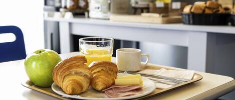A breakfast tray with croissants, ham, cheese, an apple, orange juice, and a coffee mug on a table.