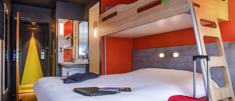 Una habitación de hotel con literas, un escritorio con espejo, una maleta y un ordenador portátil sobre la cama.