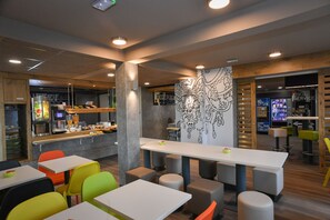 A modern cafe with colorful seating, a counter with food items, and a reception area. - Ibis Budget Saint Lo (Saint-Lo)