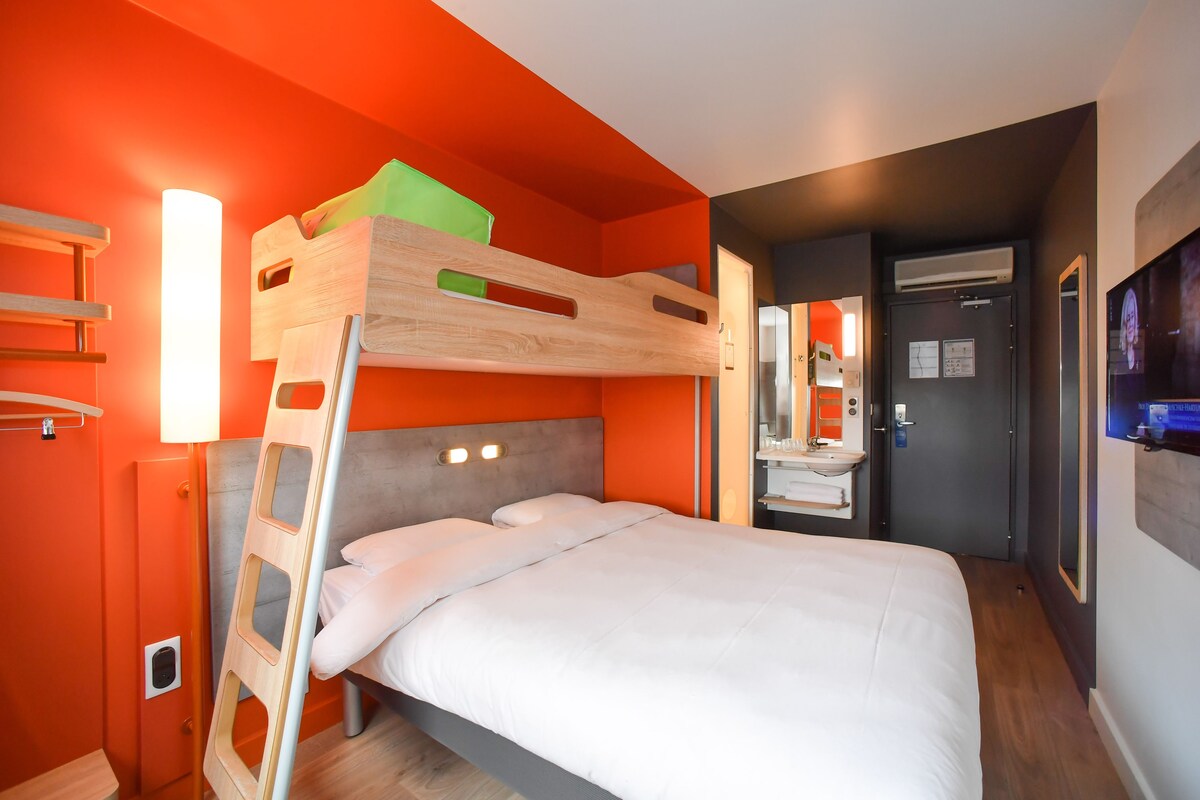 Dormitorio con literas, una escalera de madera, ropa de cama blanca y una mesita de noche pequeña.