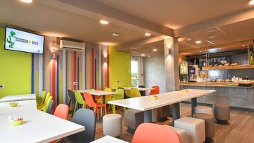 A modern restaurant with colorful chairs and tables, a bar area, and a television screen displaying an advertisement.