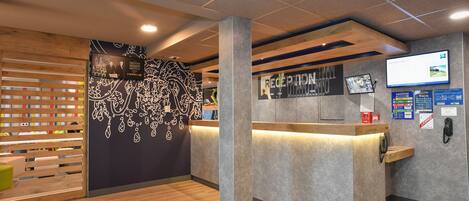 A reception area with a wooden slatted wall, a reception desk, and a mounted screen displaying information.