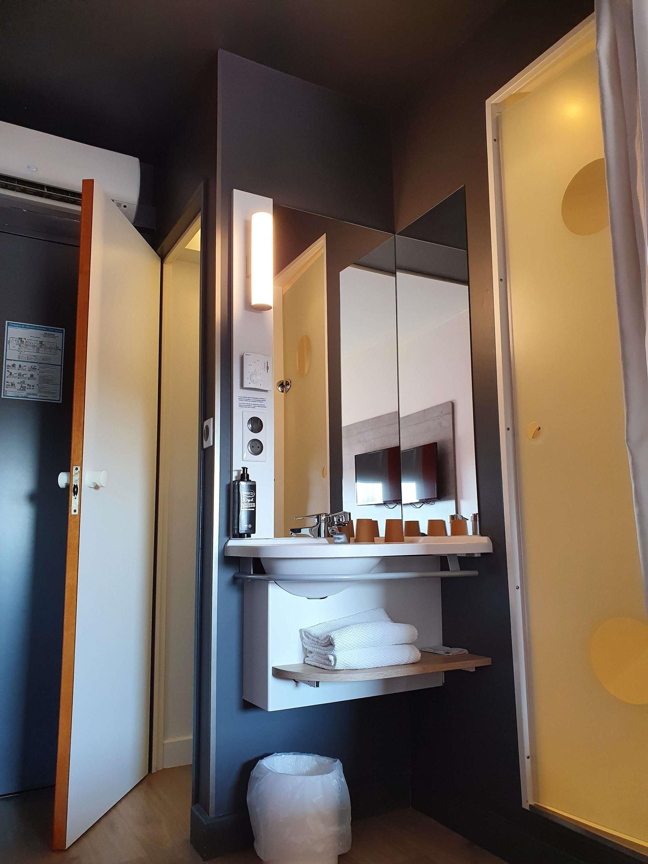 A hotel bathroom with a sink, mirror, towel rack, and a trash bin.