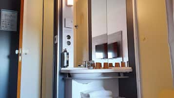 A hotel bathroom with a sink, mirror, towel rack, and a trash bin.