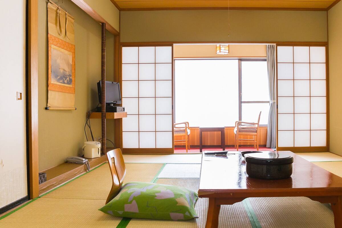 Ein traditioneller japanischer Raum mit Tatami-Boden, einem niedrigen Tisch, Kissen und Schiebetüren.