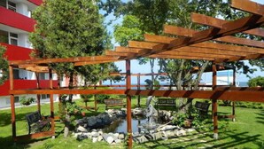 A wooden pergola structure with a small pond and rocks, surrounded by grass and trees. - Paradiso (Mangalia)