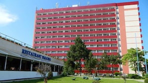 A multi-story hotel with a red and white facade, a restaurant named "RESTAURANT PARADISO" on the ground floor, and a well-maintained lawn with small trees. - Paradiso (Mangalia)