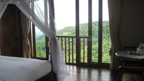 A room with a bed, a table, and a view of a forested area. - Munduk Sari Garden Villa (Munduk)