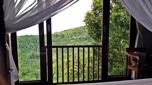 A room with a large window overlooking a forested area. - Munduk Sari Garden Villa (Munduk)