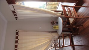 A room with a wooden floor, a dining table with chairs, and a window with curtains. - Munduk Sari Garden Villa (Munduk)