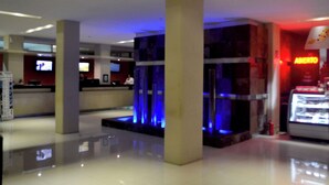Eine Hotelhalle mit einer Rezeption, einem blau beleuchteten Wasserspiel und einem Restaurant namens 'ABIERTO'.