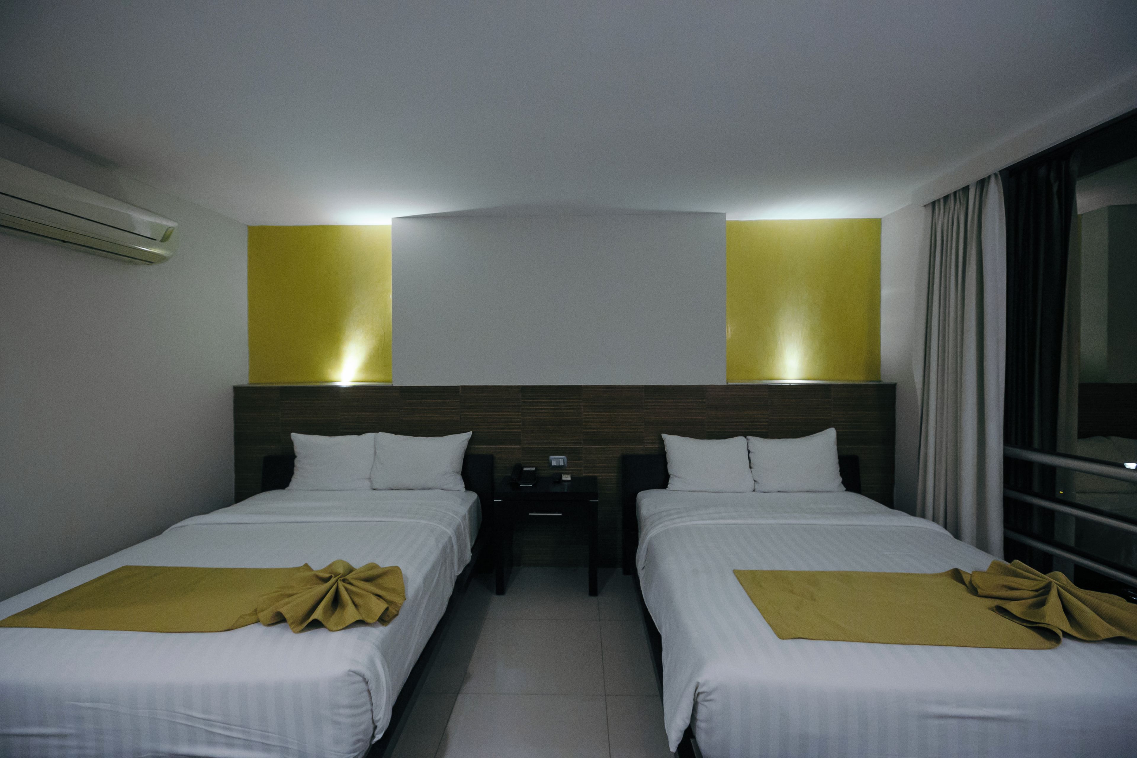 Camera d'albergo con due letti, un comodino e una finestra con tende.