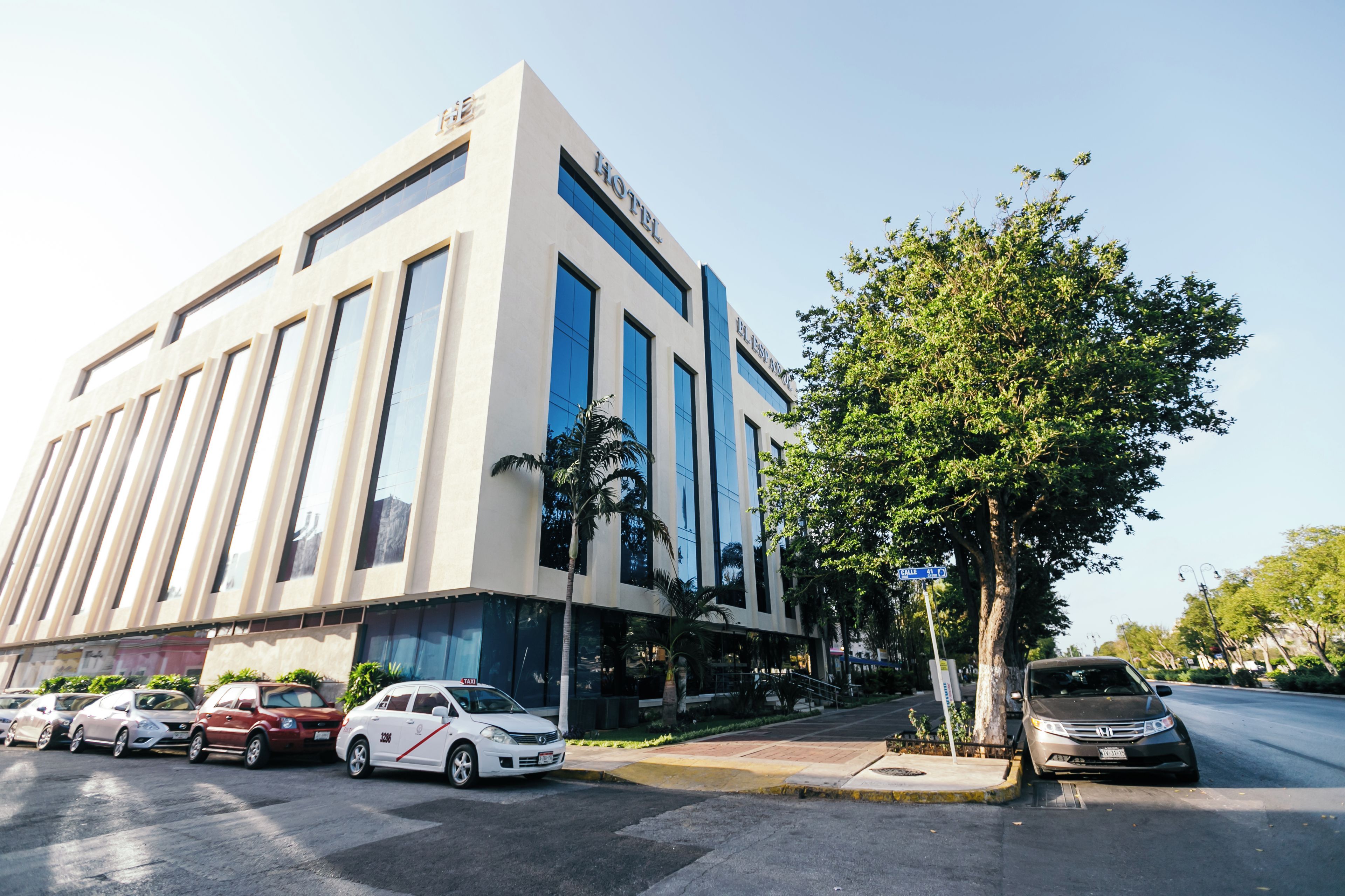 A modern building with a flat facade, large windows, and a tree in front.