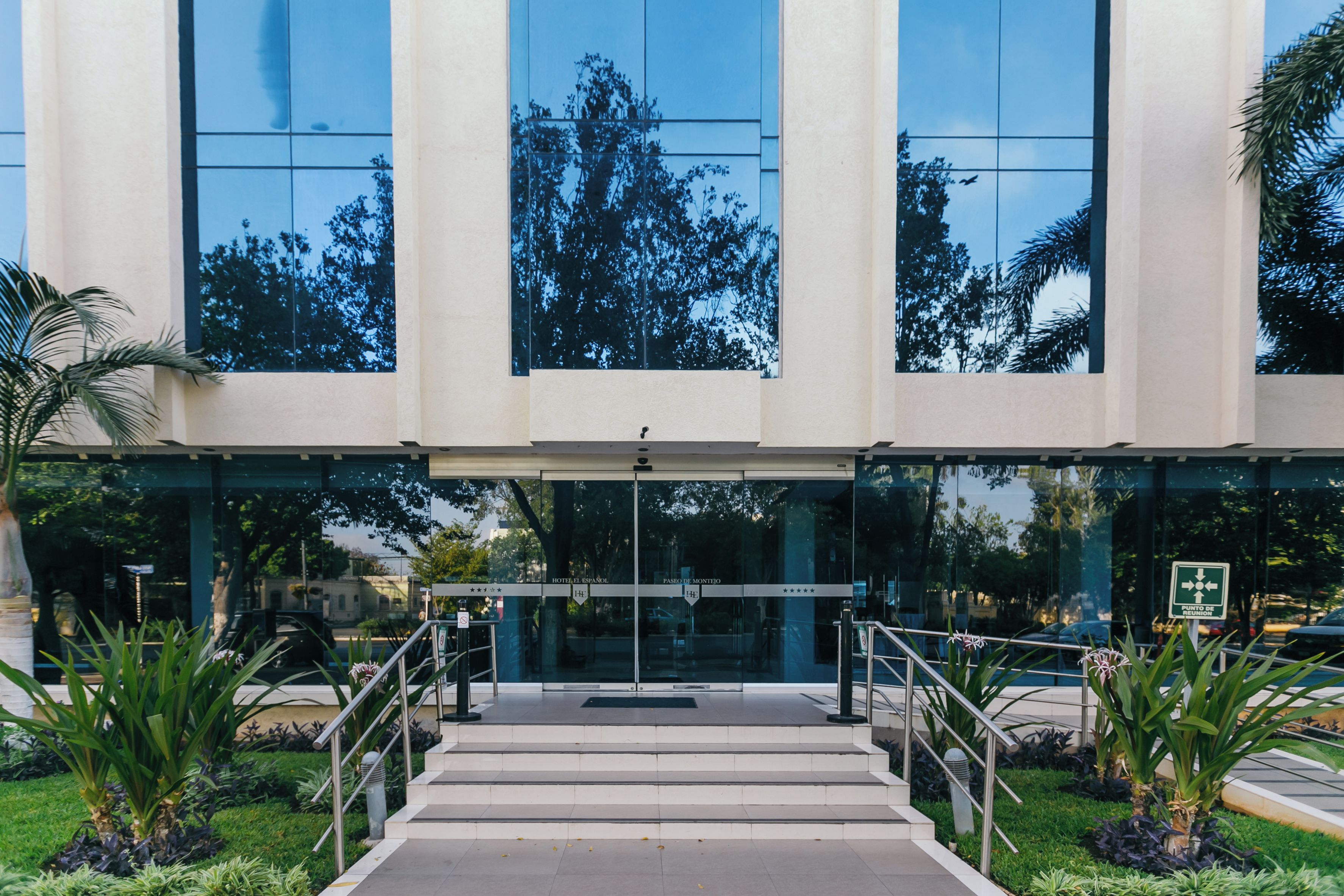 A hotel entrance with a glass facade, steps leading up to the door, and a sign indicating the hotel's name.