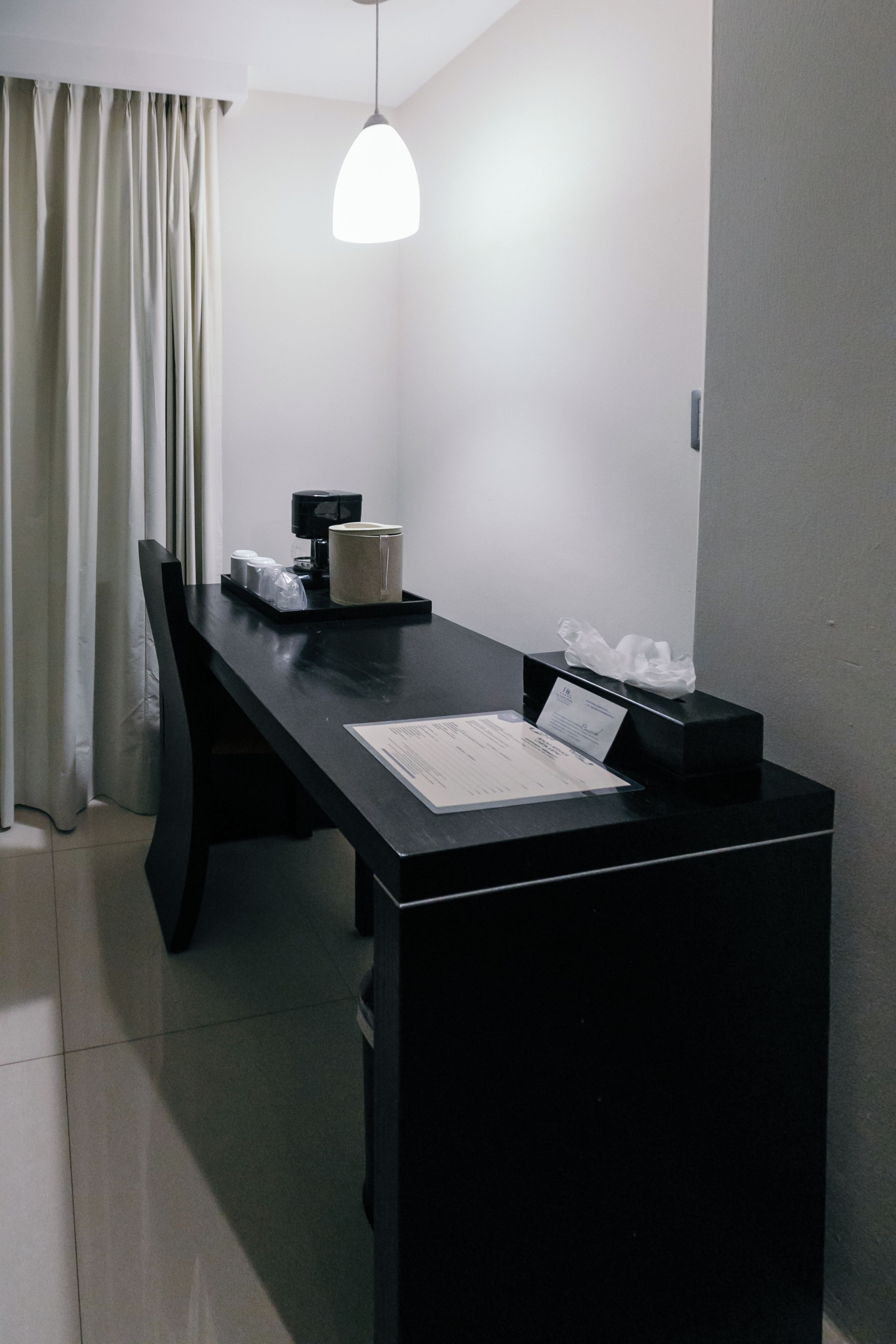 A hotel room with a black desk, a coffee maker, a tissue box, and a menu on the table.