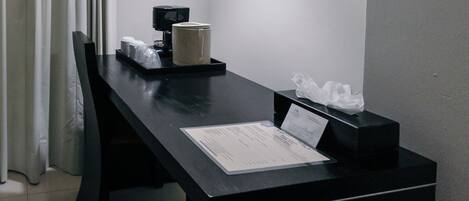 A hotel room with a black desk, a coffee maker, a tissue box, and a menu on the table.