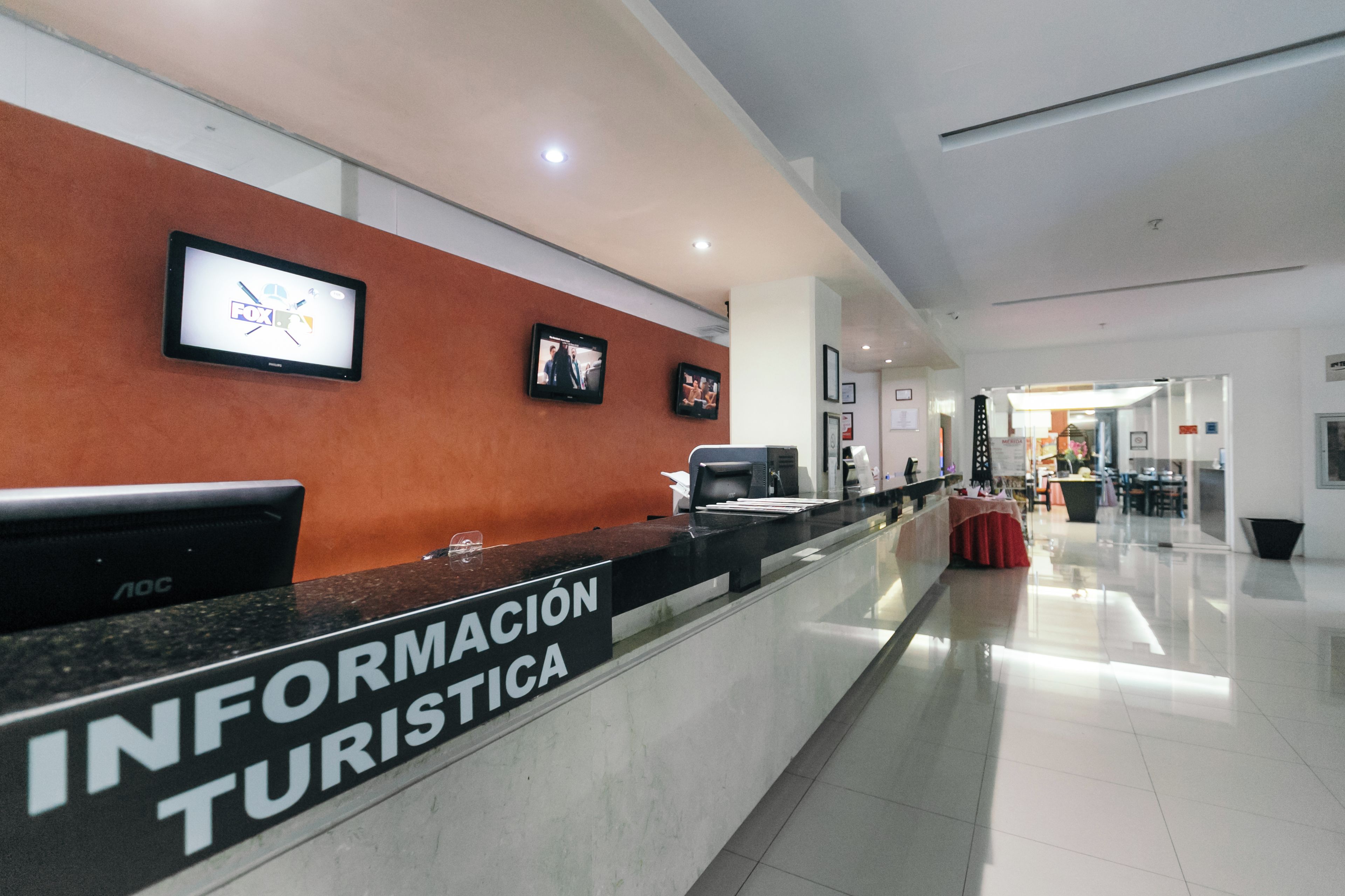 Una reception con un cartello che riporta la scritta 'INFORMACION TURISTICA' e uno schermo televisivo che mostra un notiziario.