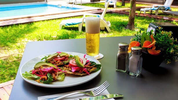 Ein Esstisch mit einer Speisenplatte, einem Bierglas, Salz- und Pfefferstreuern sowie einer Blumenkomposition.