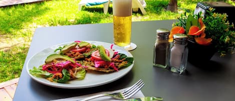 A dining table with a plate of food, a glass of beer, salt and pepper shakers, and a flower arrangement.