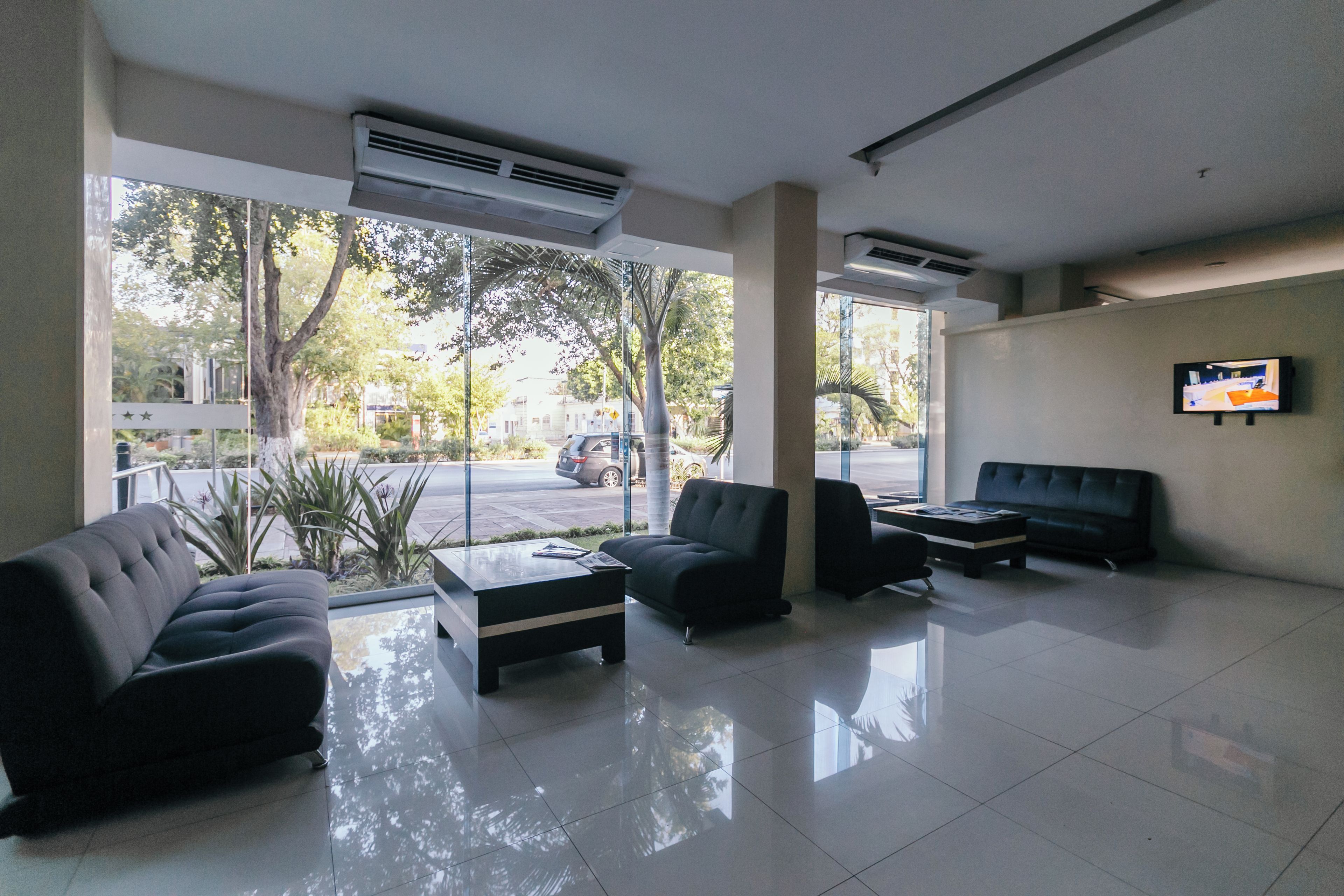A modern lobby with a glass wall, a flat-screen TV, and seating arrangements.