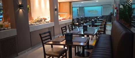 Un restaurante moderno con una zona de bufé, varias mesas de comedor y un área de estar con sofás.