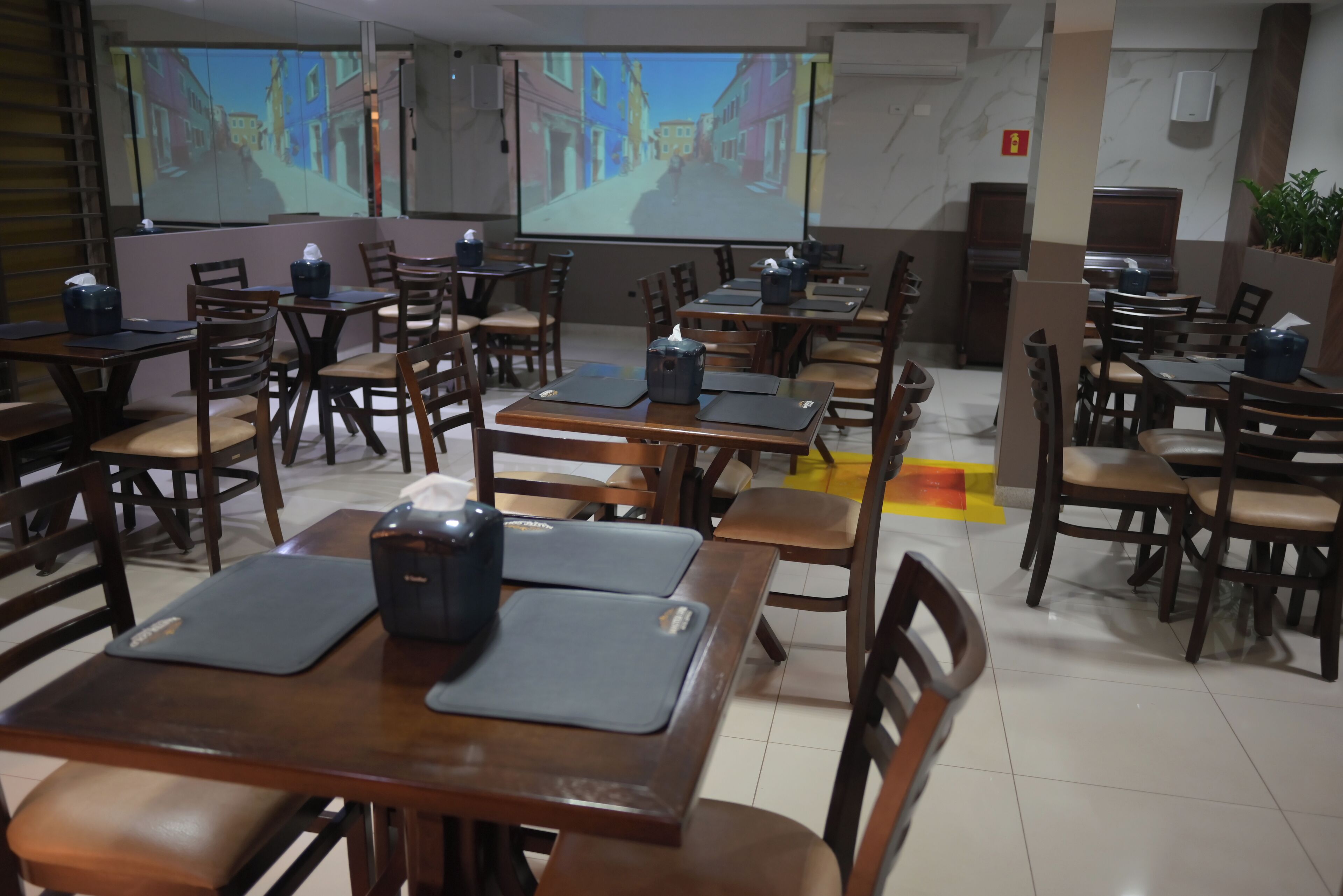 Un salón de conferencias con varias mesas y sillas, equipado con computadoras portátiles y proyectores, y una pantalla grande mostrando una presentación.