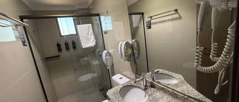 A modern bathroom with a glass-enclosed shower, a white toilet, a granite countertop with a sink, and a hairdryer mounted on the wall.