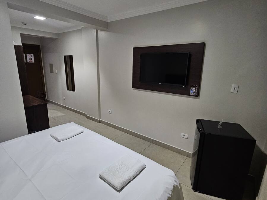 Ein Hotelzimmer mit einem großen Bett, einem an der Wand befestigten Fernseher und einem kleinen, schwarzen Schrank.