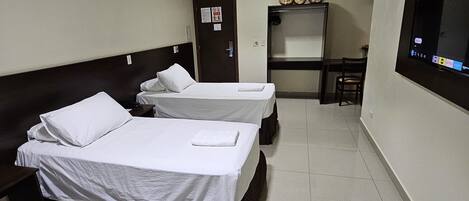 A hotel room with two single beds, a small desk, a TV mounted on the wall, and a door with a sign.