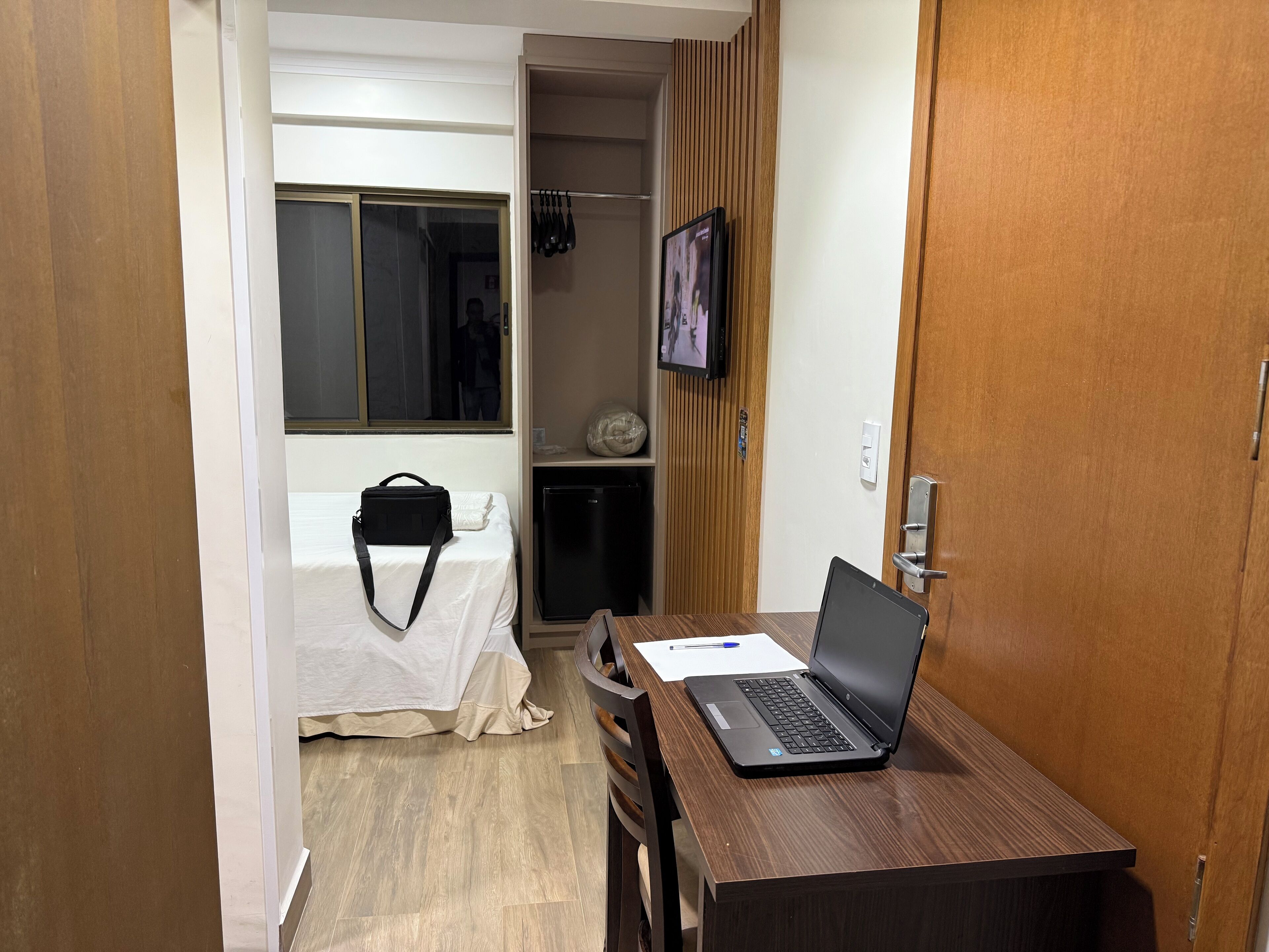 Una camera d'albergo con un letto, una scrivania con un portatile, una televisione a parete e un armadio.