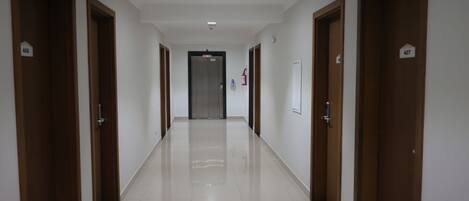 A long, narrow hallway with wooden doors on both sides, numbered 406 and 407, leading to a central elevator.