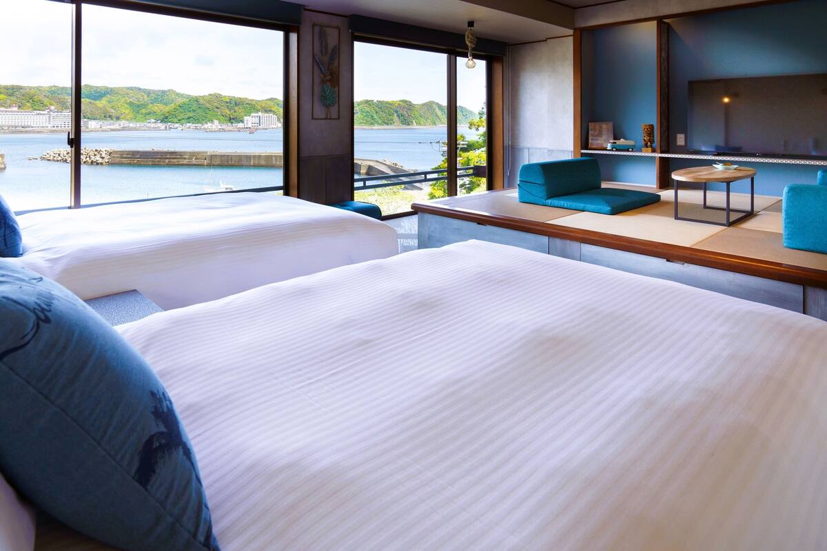 A hotel room with two beds, a view of a body of water, and a seating area with a table.