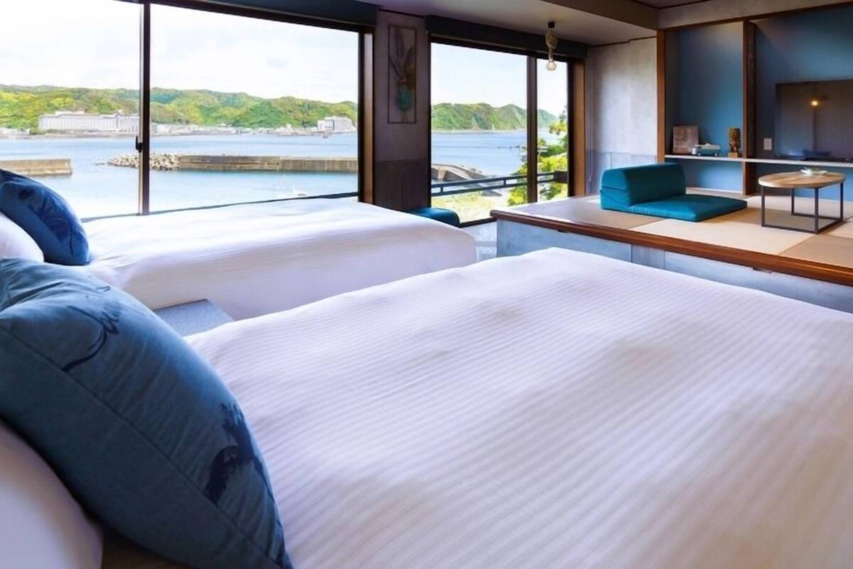A hotel room with two beds, a seating area, and a view of a body of water and greenery.
