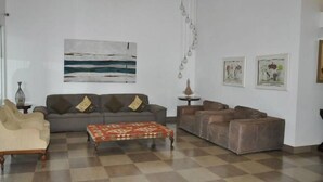 A living room with a checkered floor, a grey sofa with cushions, a patterned ottoman, and a painting on the wall. - Morubixaba Hotel (BARREIRAS)