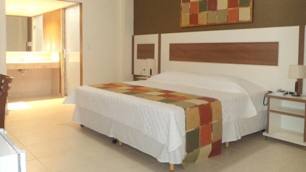 A hotel room with a large bed, a bedside table, a nightstand, a mirror, and a colorful artwork on the wall. - Morubixaba Hotel (BARREIRAS)