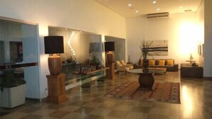 A spacious living area with a large sofa set, a coffee table, and a glass partition with lights. There are potted plants and a large artwork on the wall. - Morubixaba Hotel (BARREIRAS)