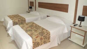A hotel room with two beds, each with a white bedspread and a patterned throw. There is a nightstand with a lamp and a phone, and a wall-mounted mirror. - Morubixaba Hotel (BARREIRAS)