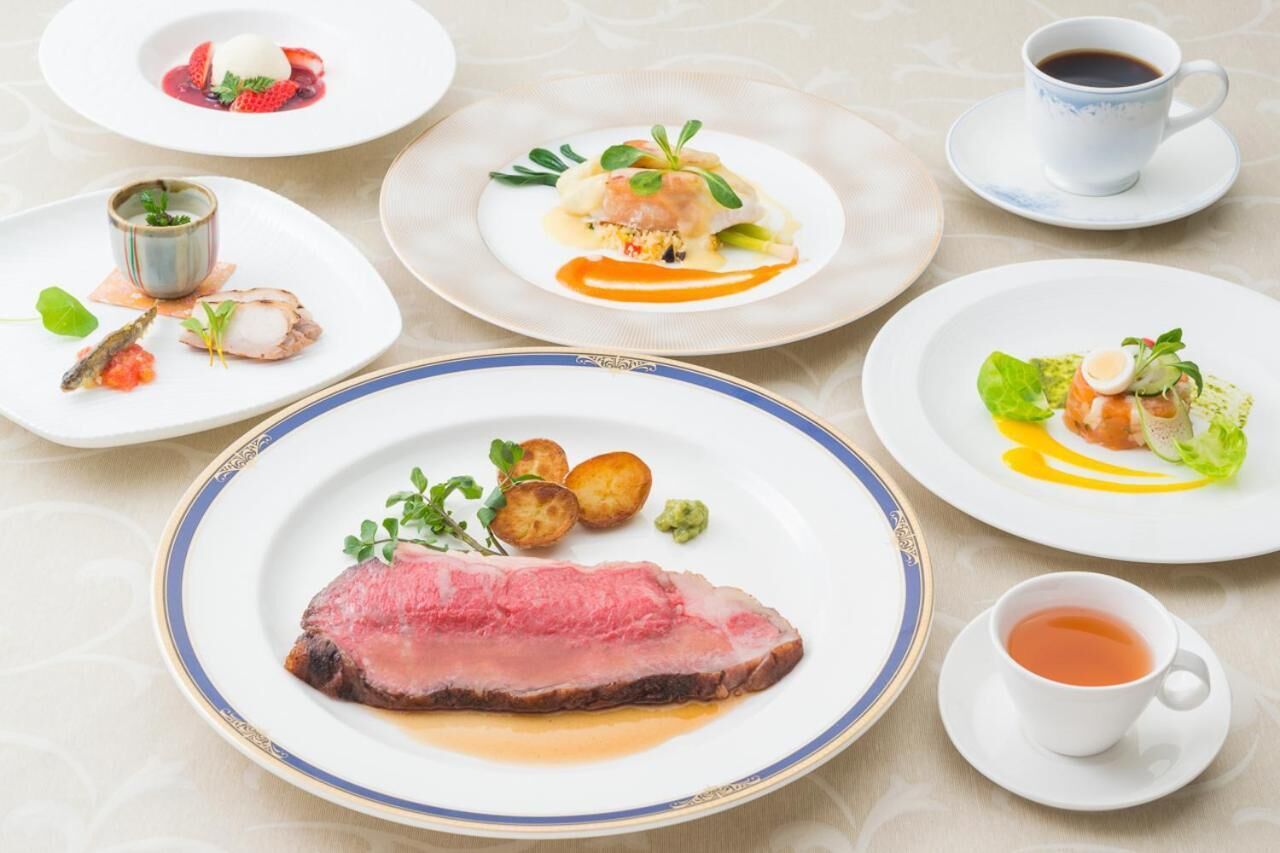 A table with various dishes, including a steak, seafood, and vegetables, along with cups of coffee and tea.
