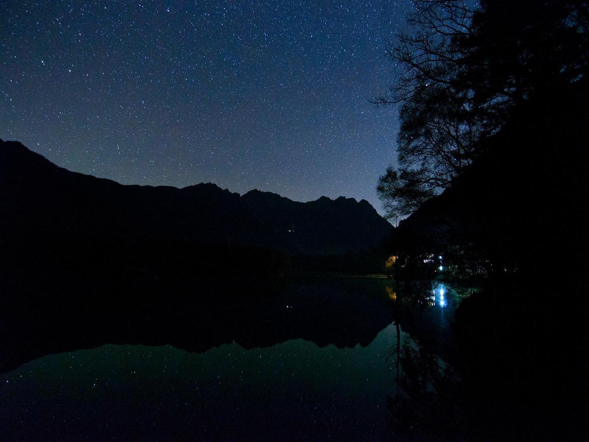 Ein sternenklarer Nachthimmel über einer Berglandschaft mit einem See, der den Himmel spiegelt.