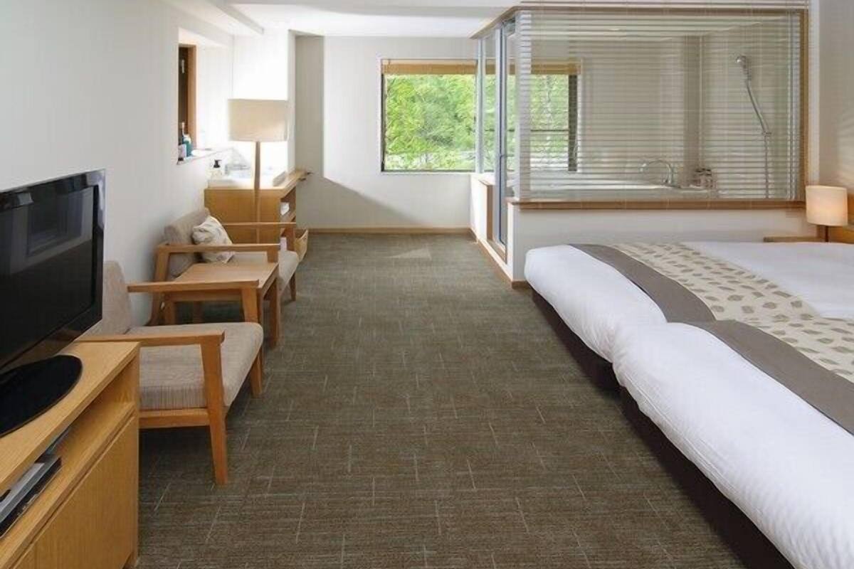 Quarto de hotel com cama, televisão, escrivaninha e janela com persianas.