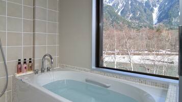 A bathroom with a bathtub, a window with a mountain view, and toiletries on the side.