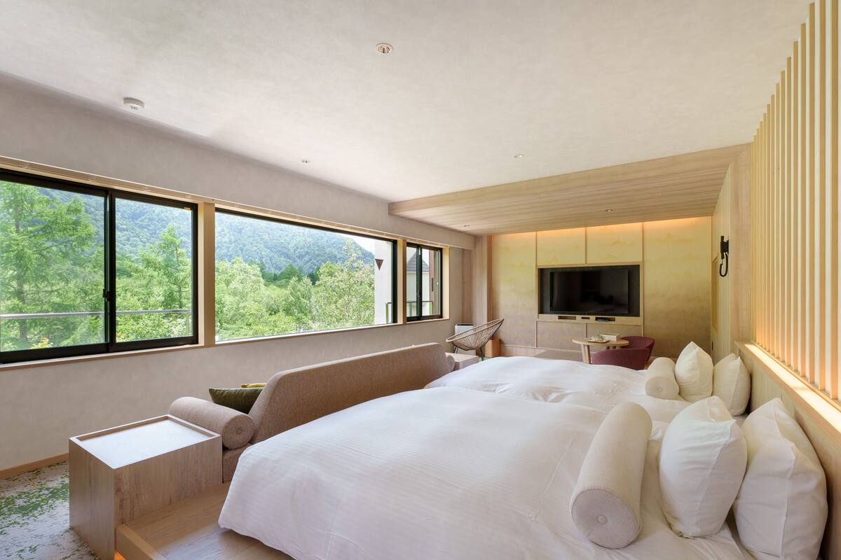 Quarto de hotel moderno com uma cama grande, televisão e vista para uma floresta.