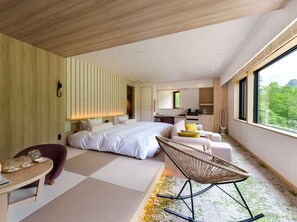 Habitación de hotel moderna con una cama grande, una zona de estar con una silla, una mesita pequeña y vistas a zonas verdes.