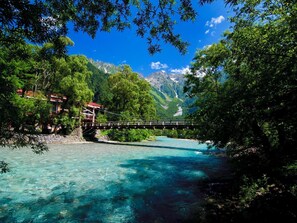 A bridge over a clear river surrounded by lush greenery and mountains. - Kamikochi Lemeiesta Hotel (Matsumoto)