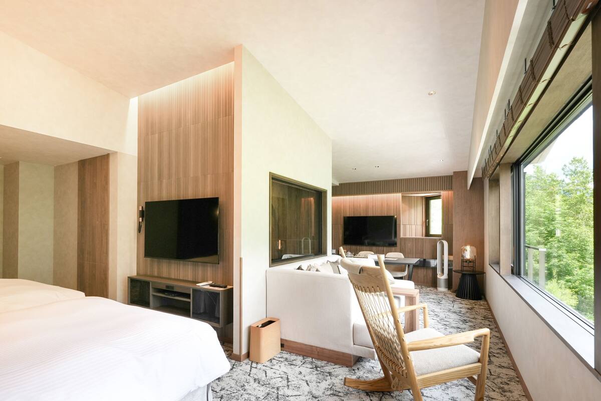 Quarto de hotel moderno com uma cama grande, área de estar com TV e vista para o exterior.
