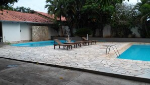 A swimming pool with lounge chairs, a stone-tiled deck, and a building with a red-tiled roof. - Pantanal Hotel (Miranda)
